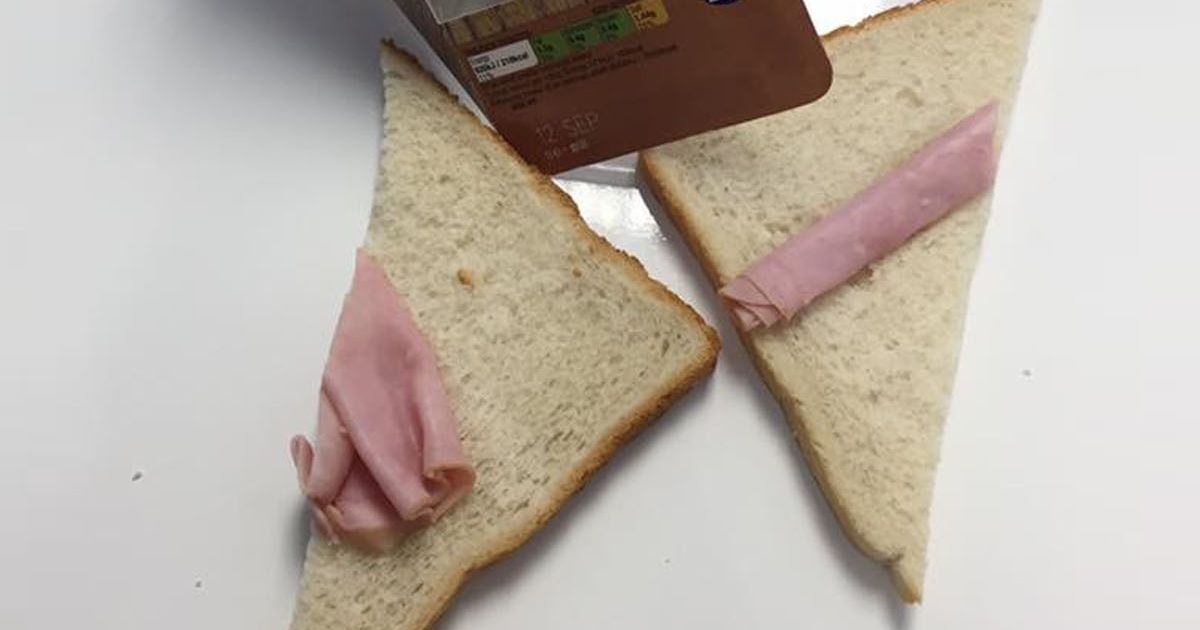 An open, un-buttered half of a sandwich showing one small folded slice of ham not covering the bread